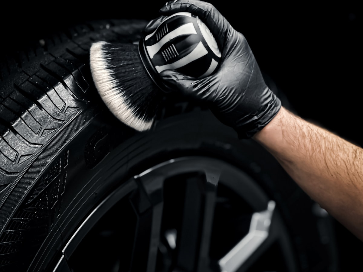 Gloved hand working a detailing brush into a wheel and tyre