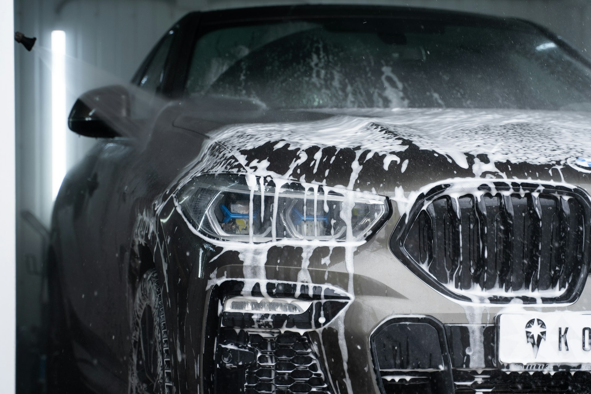 Detailer hosing foam off a car in the middle of a hand wash